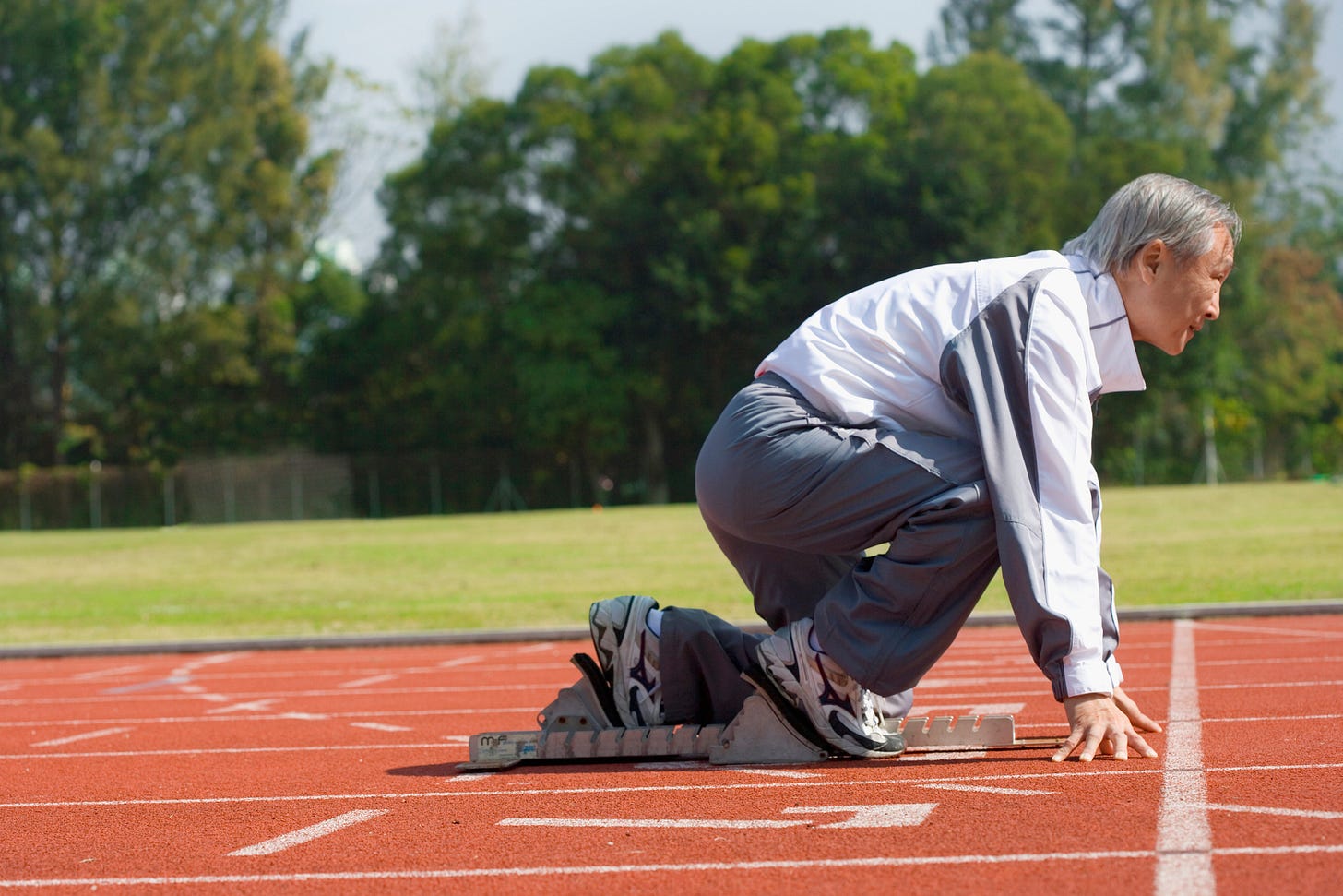 Older man in starting blocks on a track poised to sprint. Older man in starting blocks on a track poised to sprint.