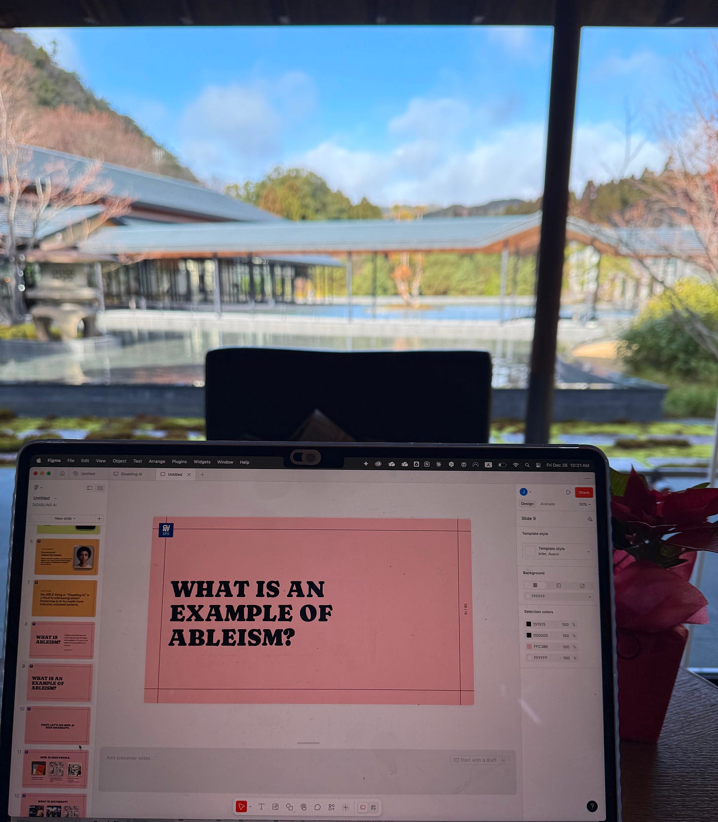 This image shows a laptop displaying what appears to be a presentation or slide deck. The current slide has a coral/salmon pink background with bold black text that reads "WHAT IS AN EXAMPLE OF ABLEISM?"  The laptop is positioned facing a scenic outdoor Japanese garden in Kyoto. Through the windows, there s beautiful natural landscape with trees, hills, and what appears to be a body of water or pool area with a modern architectural structure featuring a distinctive roof design.
