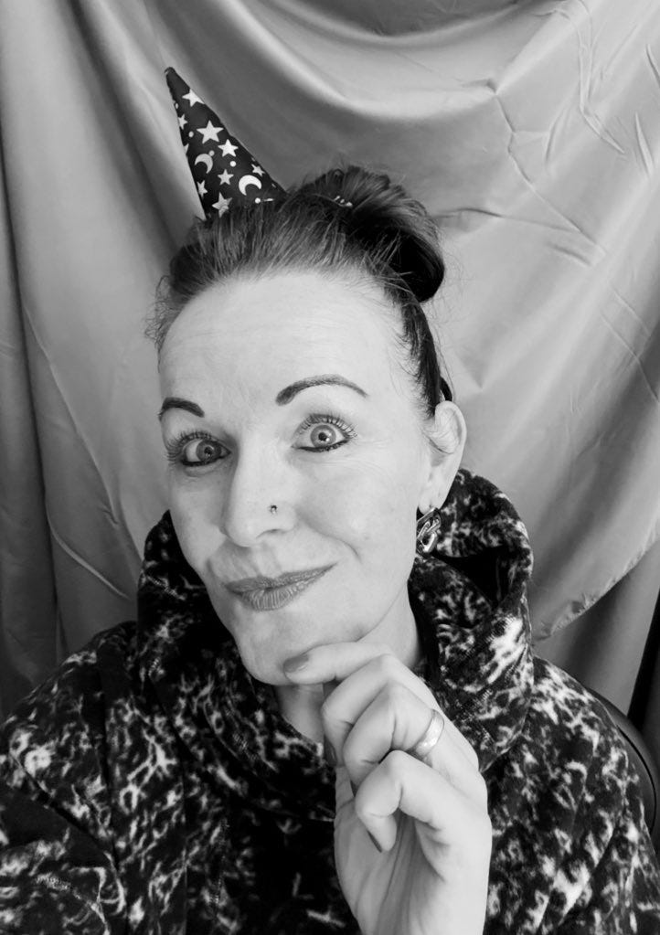 Georgina Dean, wearing a party hat and a leopard-print hoodie, smiles as she holds up her new glasses case, which is black with a floral pattern and a whimsical skeleton.