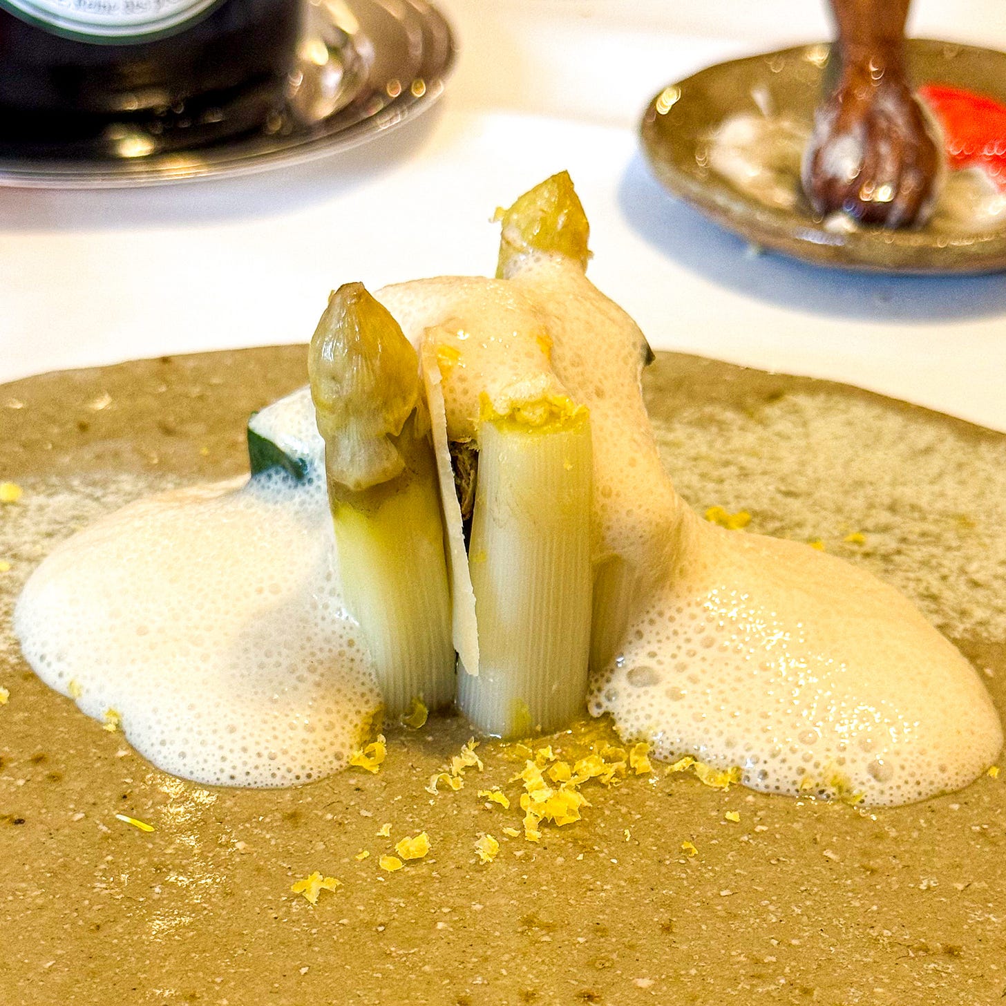 Two upright white asparagus spears wrapped in sea lettuce under a pale anchovy foam, dusted with lemon zest, at Datil in Paris. Two upright white asparagus spears wrapped in sea lettuce under a pale anchovy foam, dusted with lemon zest, at Datil in Paris.