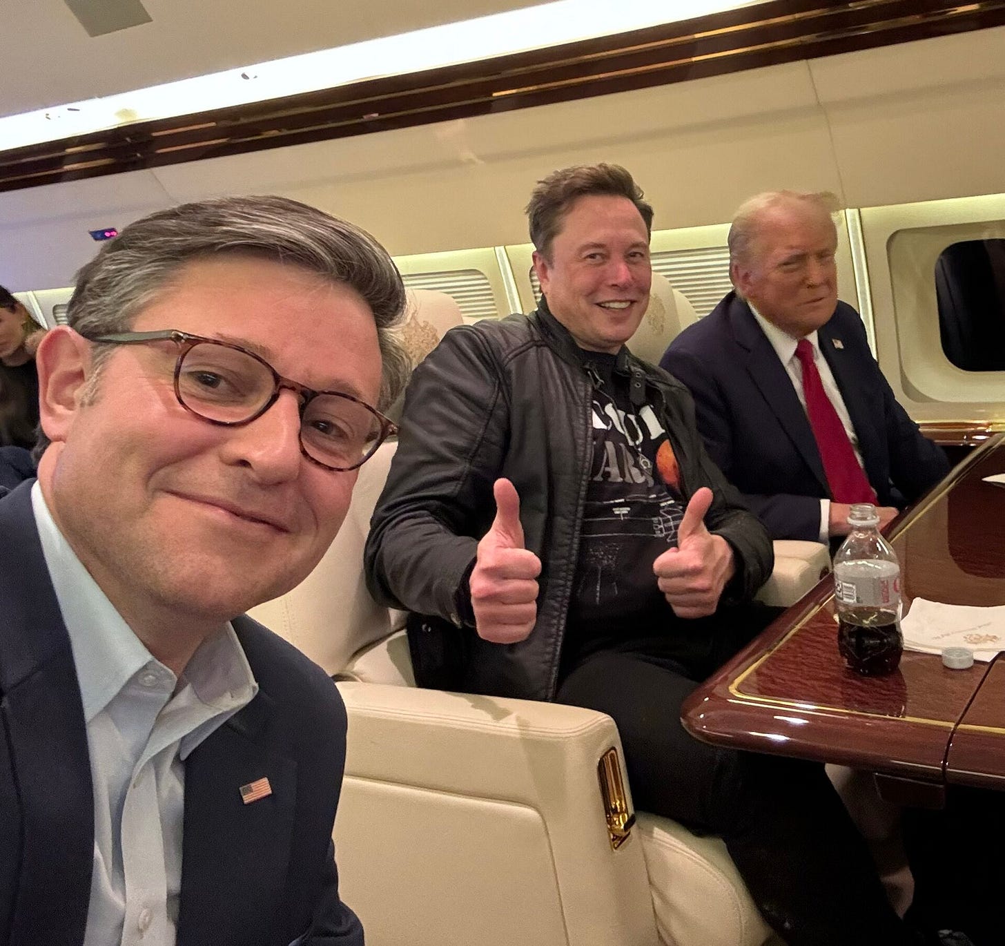 Mike Johnson takes a selfie on a plane; Trump is mugging in the background, as is Elon Musk, who has two thumbs up