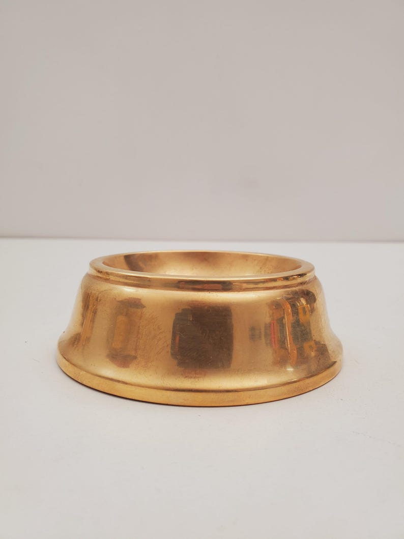 May include: A gold metal decorative stand with a round top and a slightly flared base.