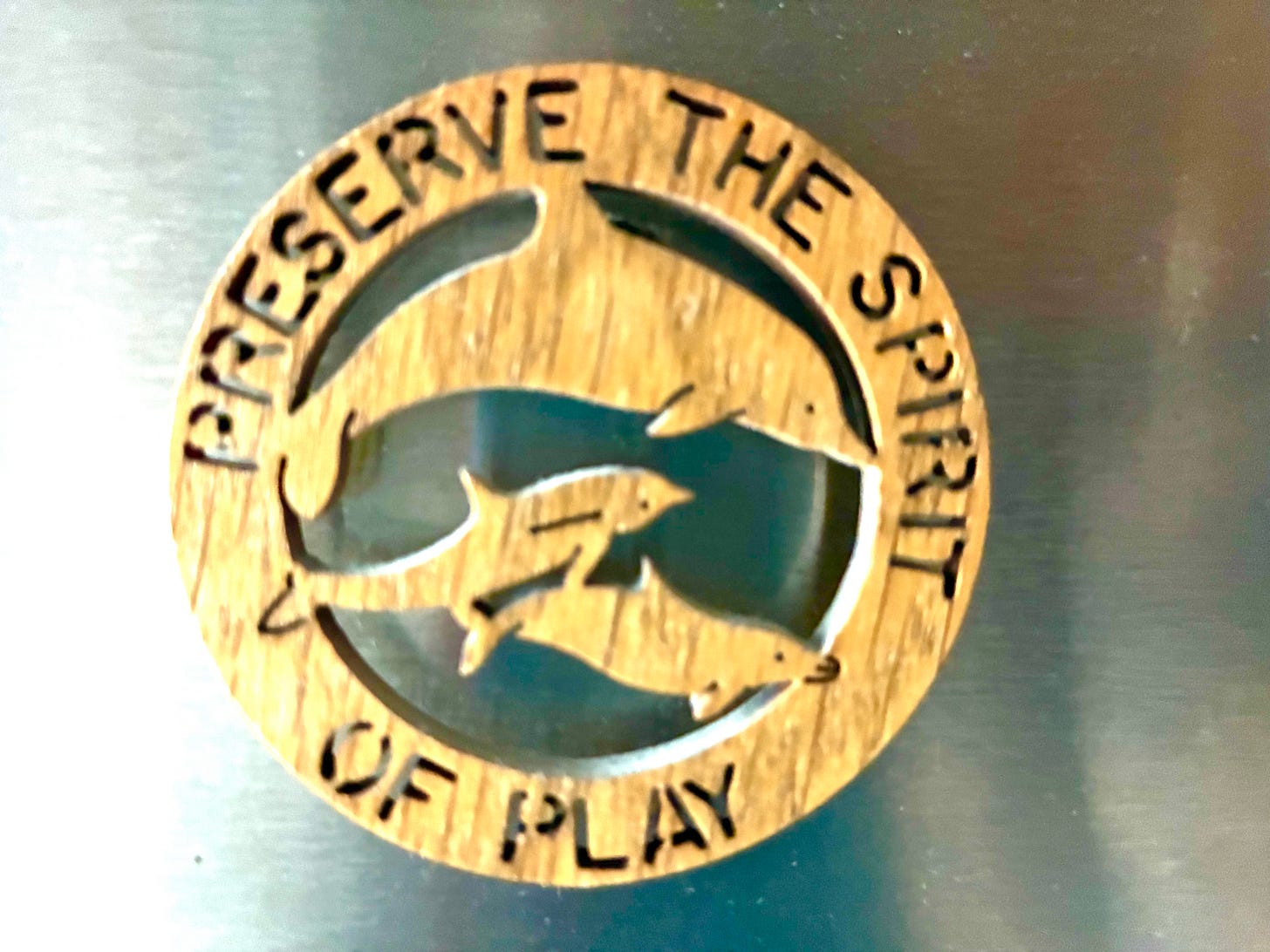 wooden refrigerator magnet with dolphins surrounded by the words "preserve the spirit of play"