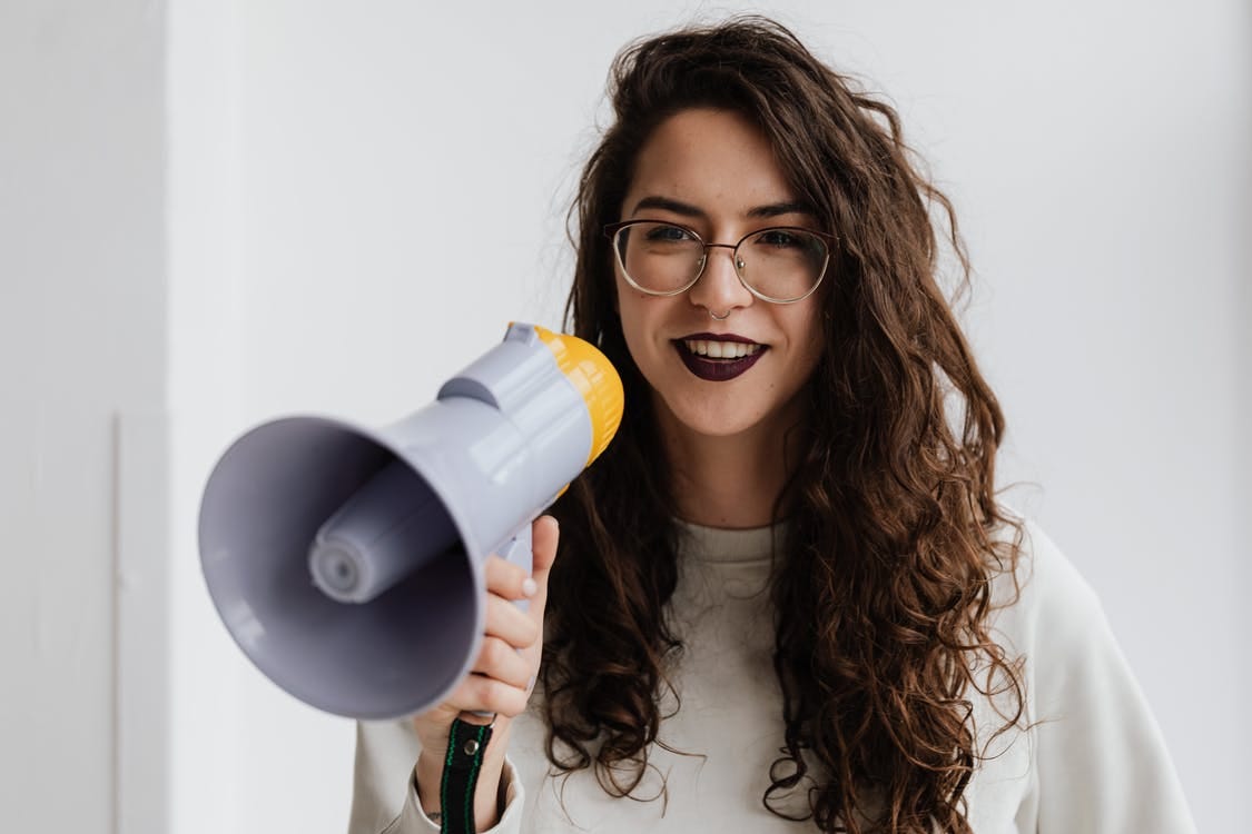 Woman in white long-sleeved shirt holding a grey megaphone.