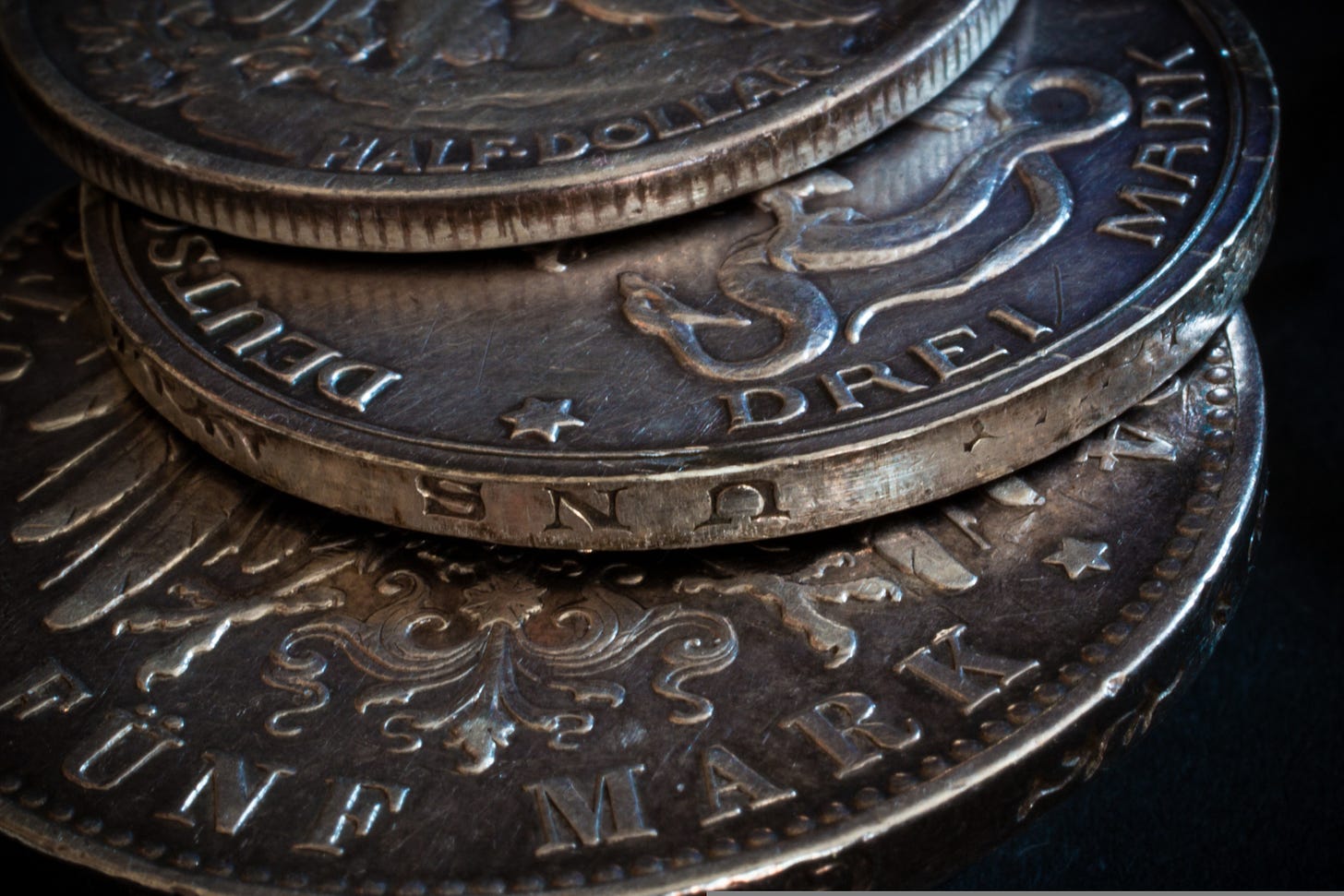 Artistic close-up of overlapping silver coins with visible engravings, letters, and decorative patterns on their surfaces, photographed with shallow depth of field. Artistic close-up of overlapping silver coins with visible engravings, letters, and decorative patterns on their surfaces, photographed with shallow depth of field.
