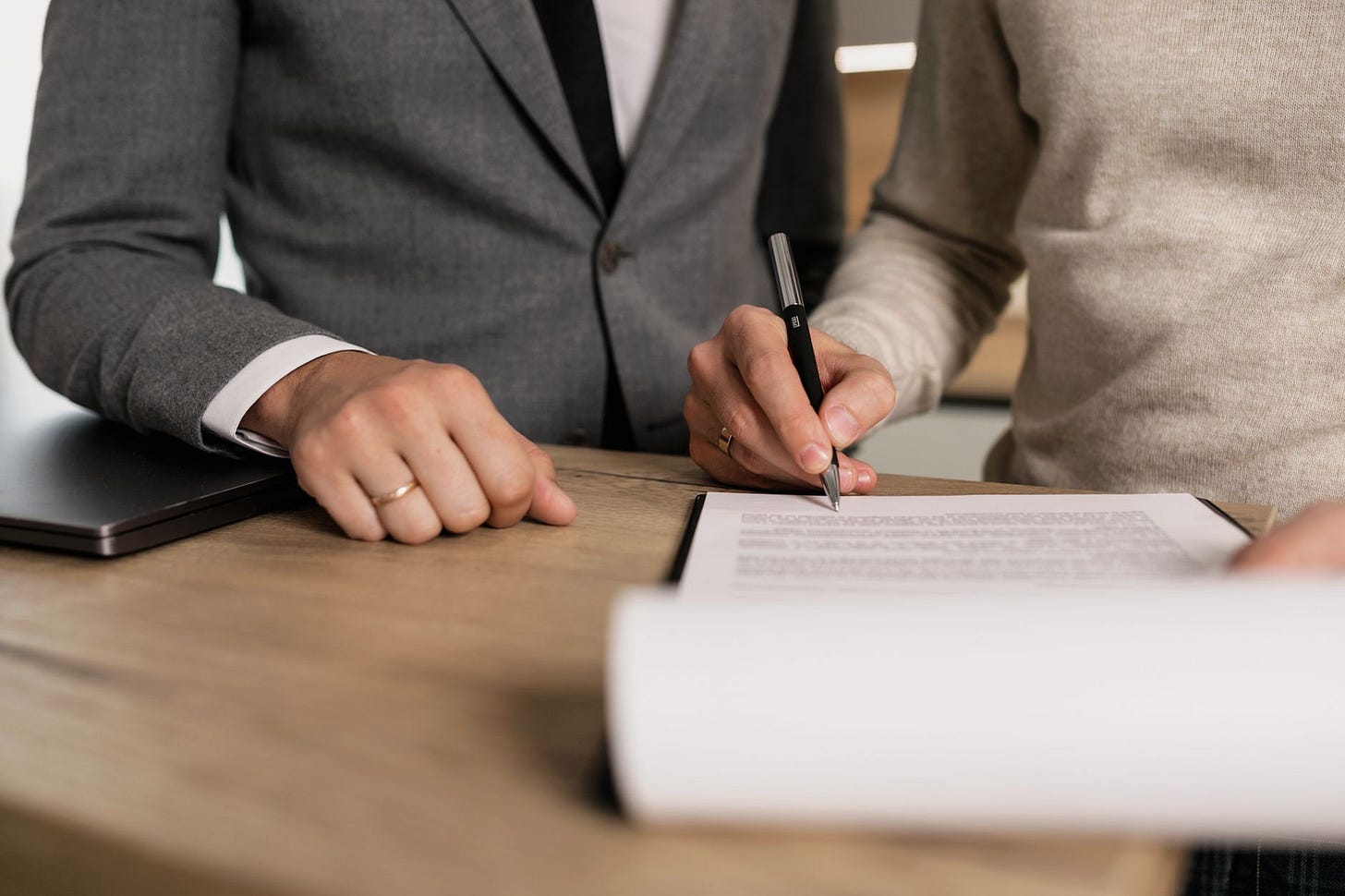 Photo by Alena Darmel on Pexels Close-up of businessmen signing documents at a wooden table in an office. (stock photo)