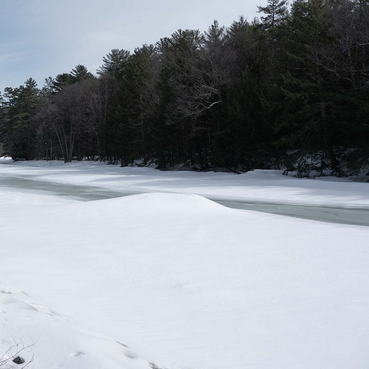 Four photographs of a snow covered rock in the middle of an icy river, which is melting so there is water flowing in the third and forth images.