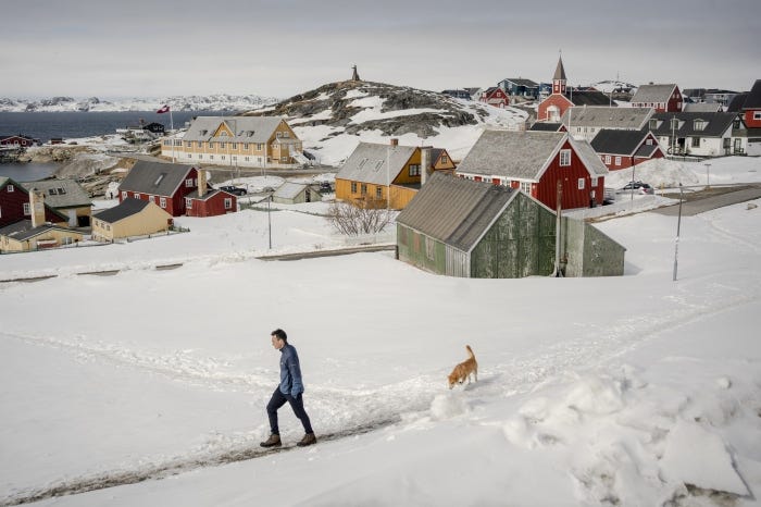 A man walks his dog in a snow-covered Nuuk city center.