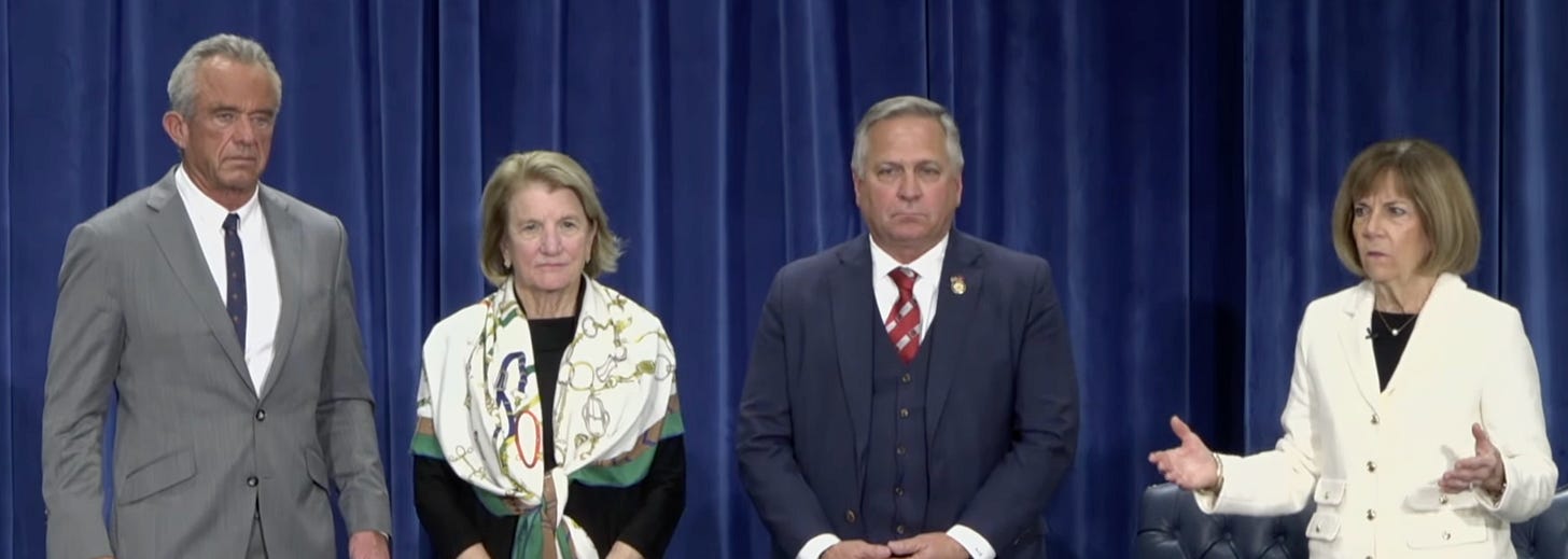 4 white public officials stand on a stage against a blue curtain backdrop. Each looks miserable in a different way. 4 white public officials stand on a stage against a blue curtain backdrop. Each looks miserable in a different way.