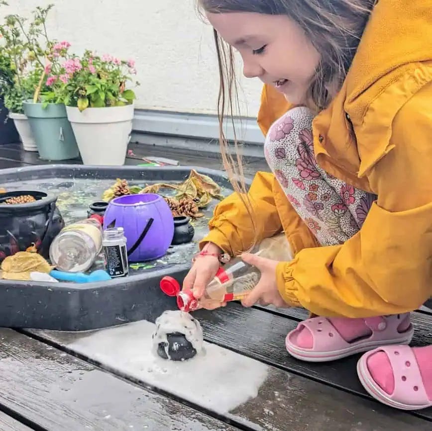 a 7 year old girl smiles as she adds vinegar to a mini cauldron to make a fizzy potion