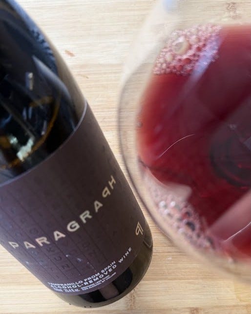 Overhead shot of a Paragraph alcohol-removed Tempranillo bottle beside a glass of deep ruby wine on a wooden table.