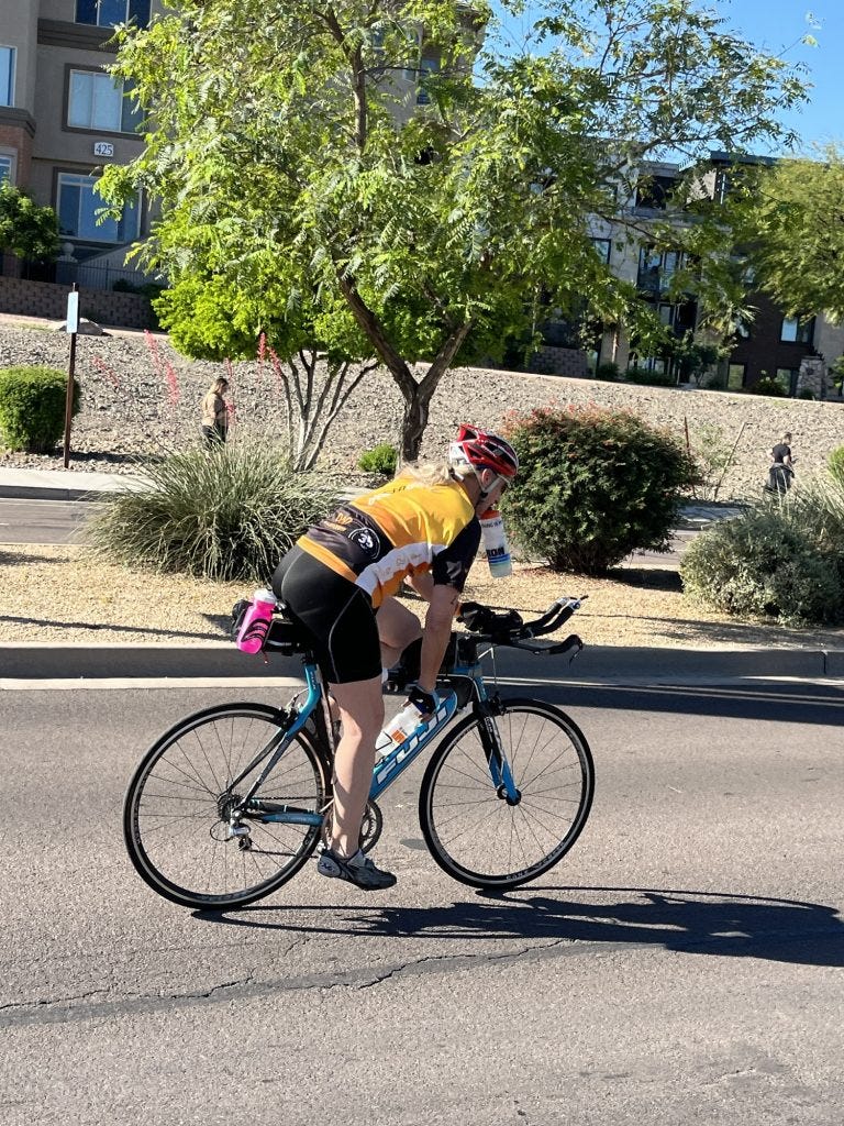 Cyclist on a blue bike cycling down a road lined with trees. She has a yellow cycling jersey and a red helmet. Cyclist on a blue bike cycling down a road lined with trees. She has a yellow cycling jersey and a red helmet.