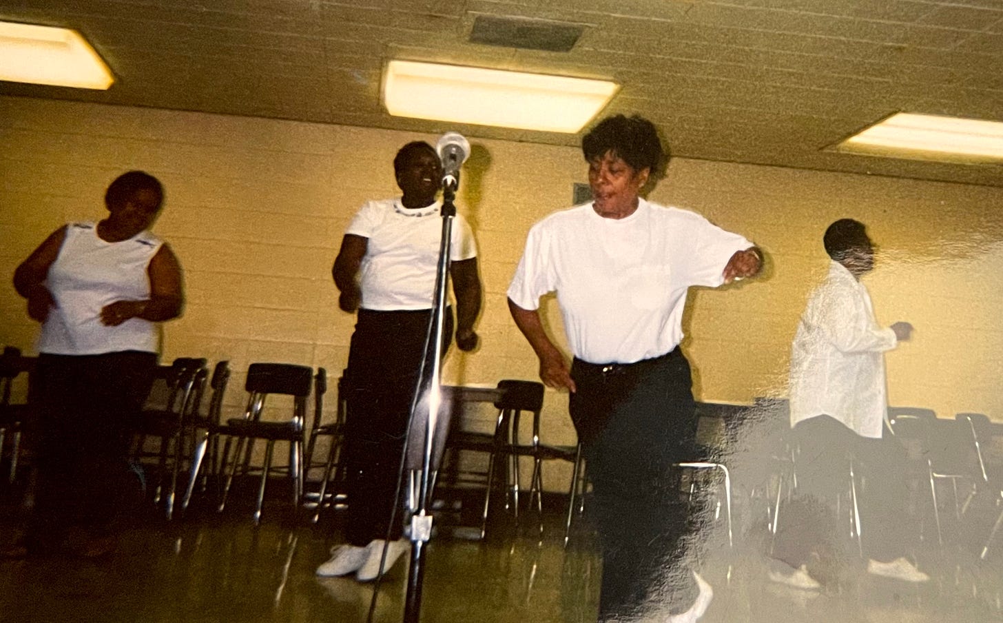 Jemar's mom dancing in black jeans and a white t-shirt along with three other women in the background Jemar's mom dancing in black jeans and a white t-shirt along with three other women in the background
