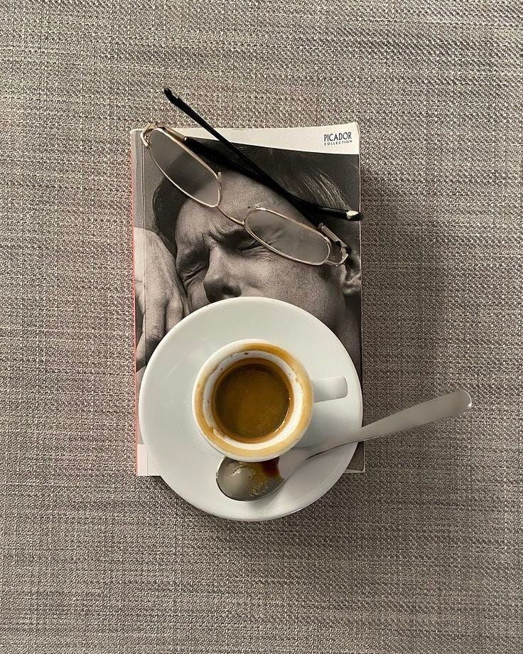 This may contain: a cup of coffee sitting on top of a white saucer next to a book