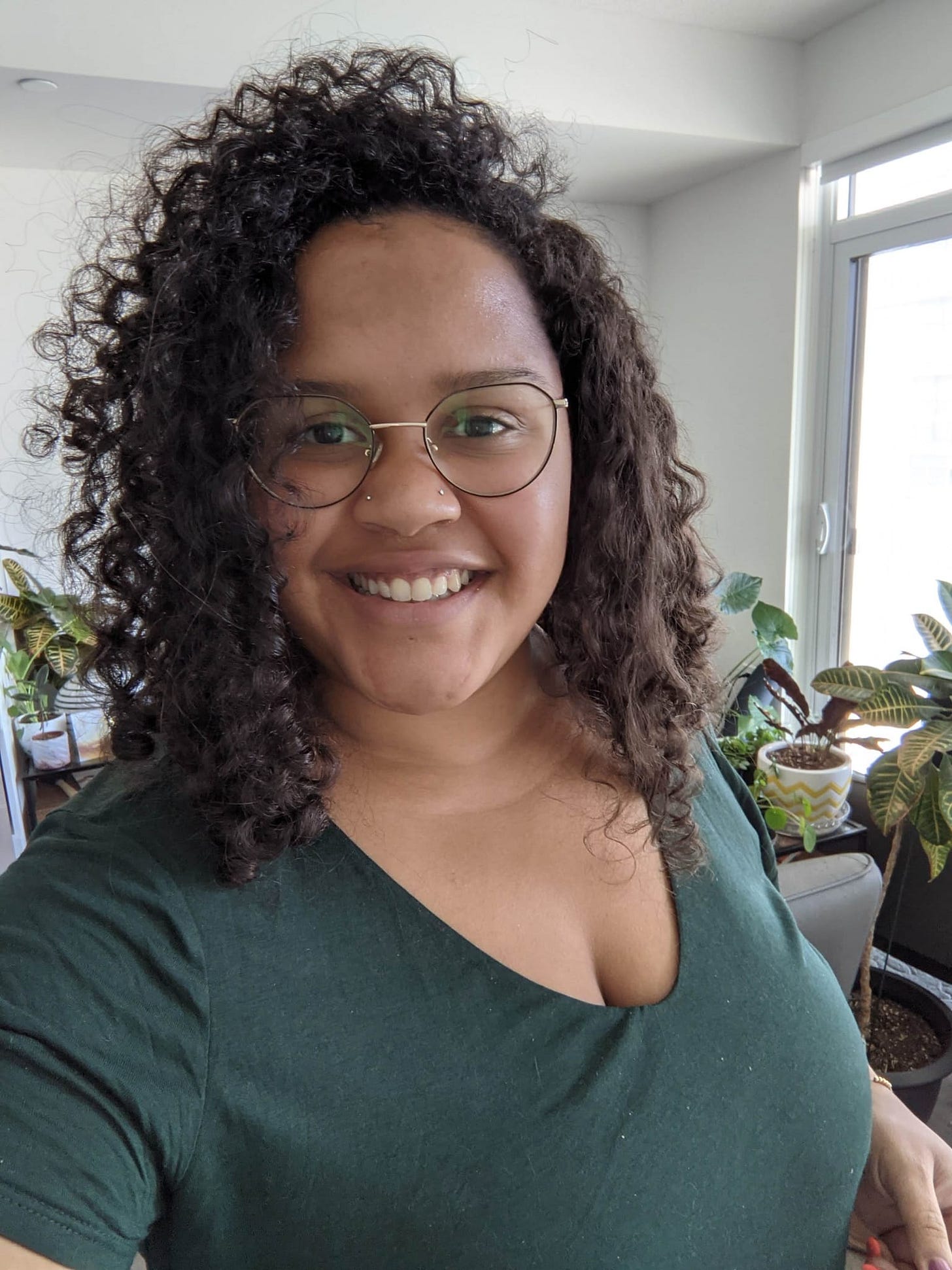 A portrait photo of Danielle Nadine Pierre wearing a green shirt with plants in the background.