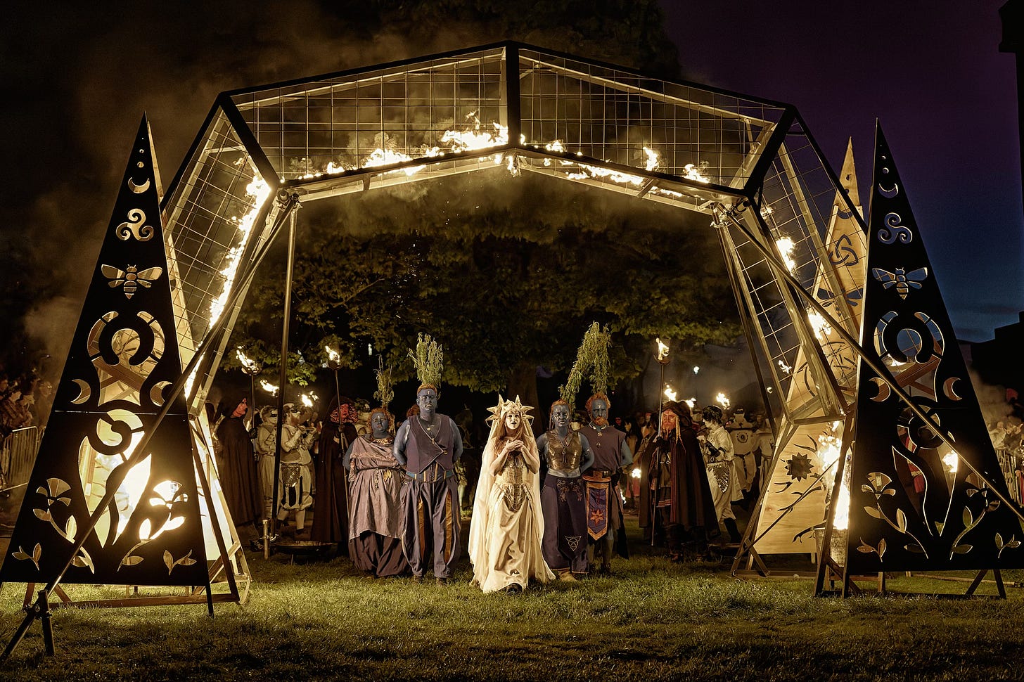 This documentary fieldwork photograph shows the May Queen leading her procession through the flaming purification archway. Beltane, Edinburgh 2026