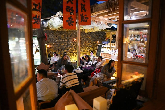 People sitting and chatting in a cosy, warmly lit room with wooden decor after a music performance at a ‘youth retirement home’. People sitting and chatting in a cosy, warmly lit room with wooden decor after a music performance at a ‘youth retirement home’.