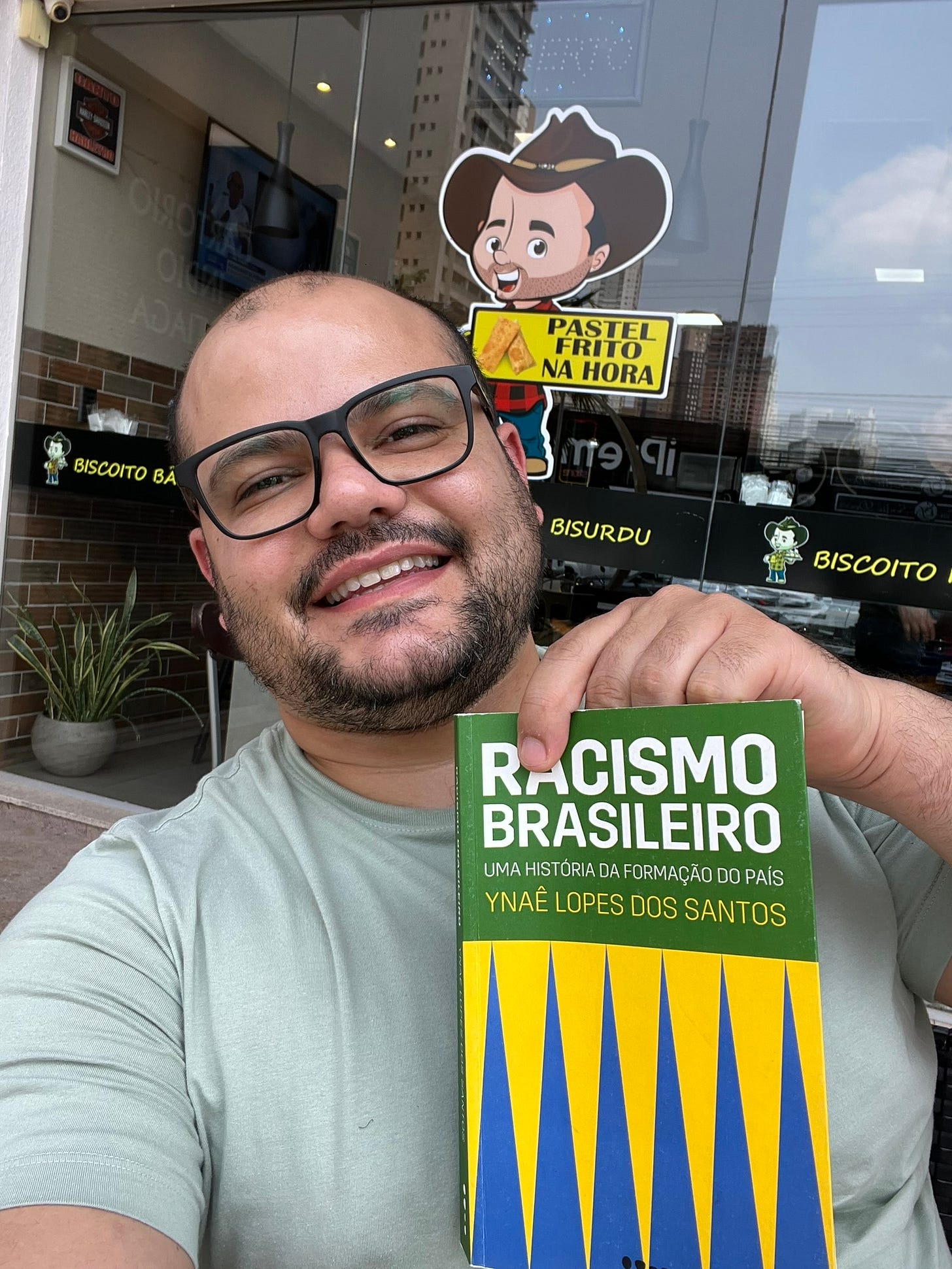 Homem de óculos sorrindo segura o livro Racismo Brasileiro