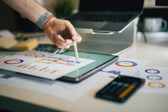 Photo of a person creating a report using graphs and various digital devices.