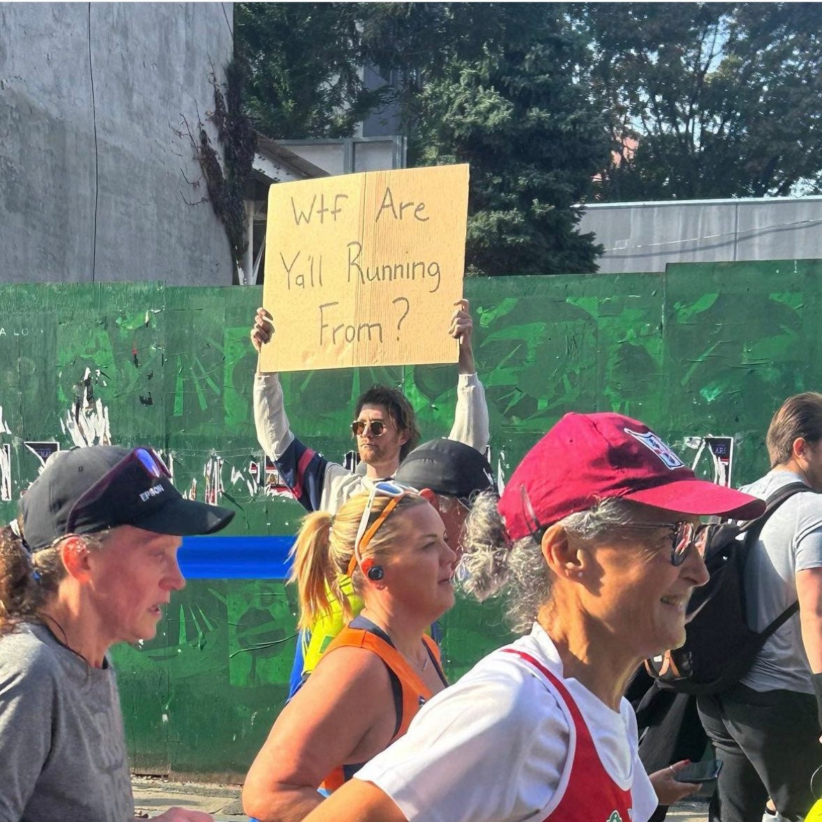 Man holding sign beside marathon runners that reads "WTF Y'all running from?" Man holding sign beside marathon runners that reads "WTF Y'all running from?"