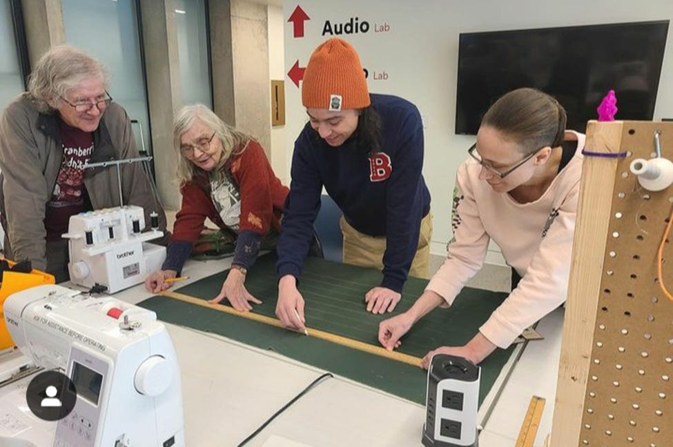 Four people gathered around a table with sewing machines, a green mat, and a ruler.