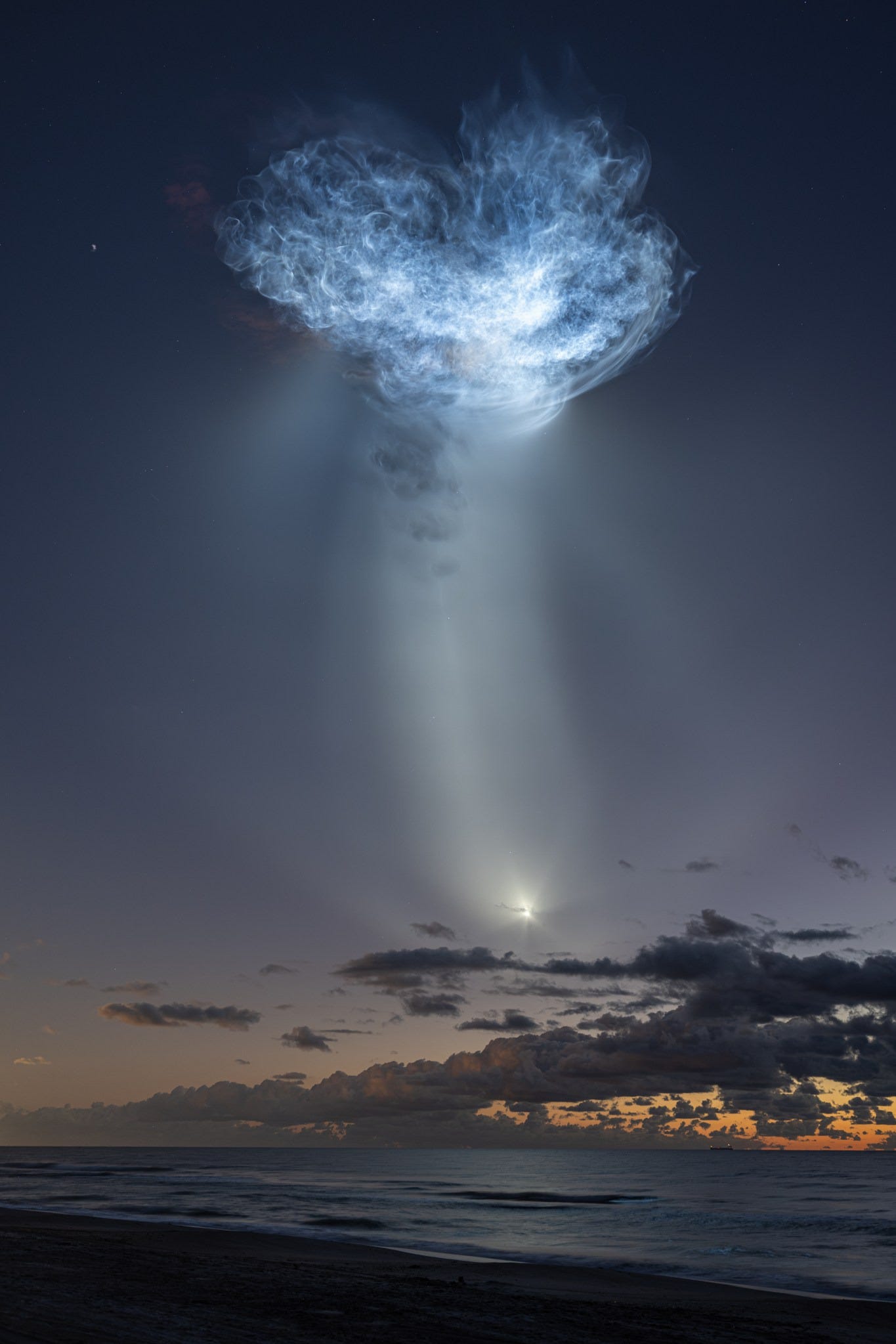 The exhaust plumes of a SpaceX Falcon 9 rocket carrying the company’s Dragon spacecraft are seen illuminated by sunlight against the predawn sky.