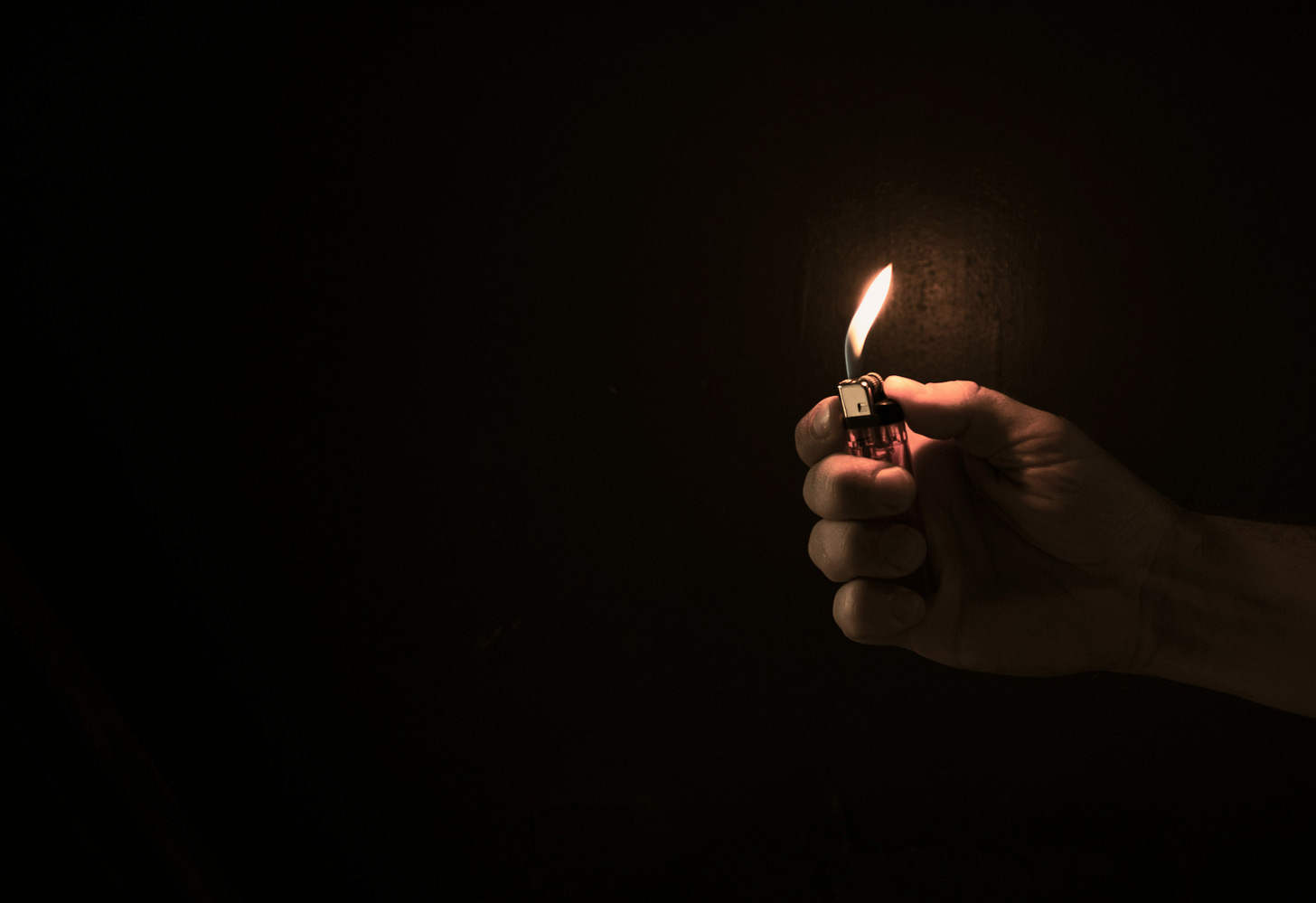 A hand holding a lighter against a black background.