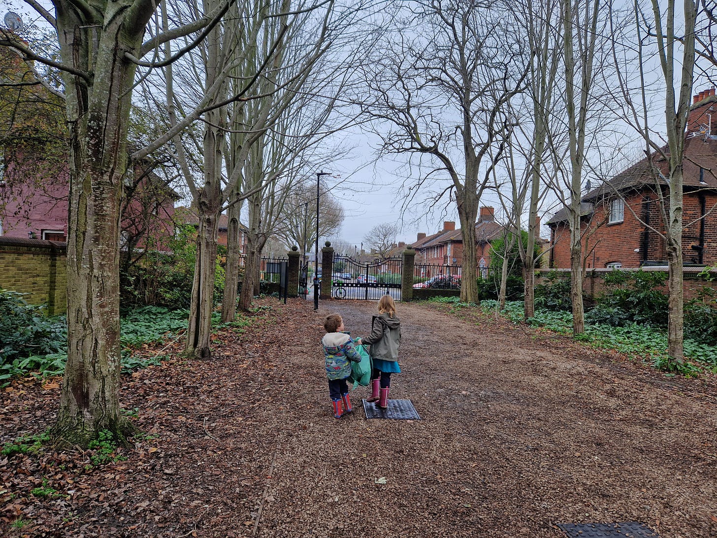 two small children carrying a rubbish bag through a park. we can only see the backs of their heads