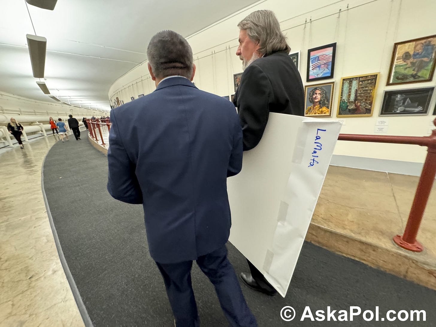 Two men walk down tunnel, one carrying a chart with art work on walls. Photo: Matt Laslo © www.askapolpolitics.com Two men walk down tunnel, one carrying a chart with art work on walls. Photo: Matt Laslo © www.askapolpolitics.com