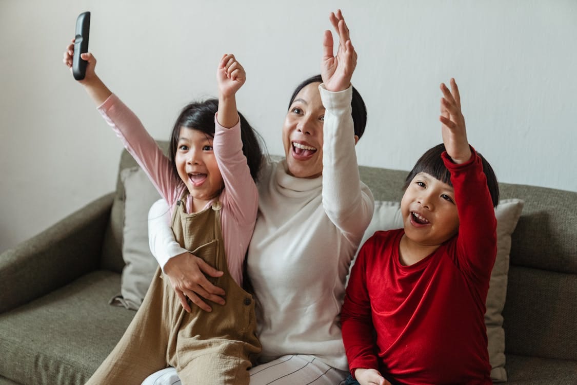 Free Excited mom and kids celebrating a victory together on the sofa. Stock Photo
