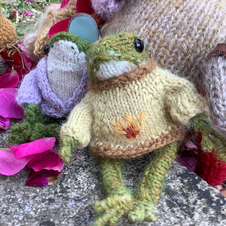 Knitted toys under a red rose bush surrounded by fallen petals