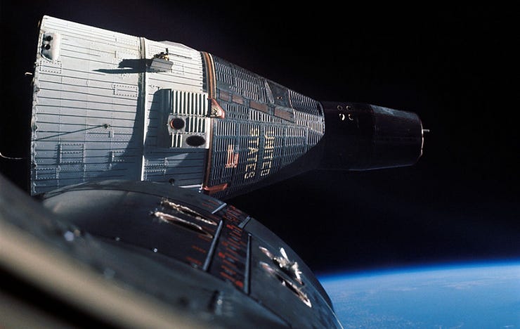 Two spacecraft docked in orbit above Earth, with a visible curvature of the planet in the background. Spacecraft are gray with black and orange details. Two spacecraft docked in orbit above Earth, with a visible curvature of the planet in the background. Spacecraft are gray with black and orange details.