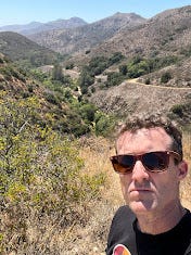 Photos of a desert hike featuring pictures of brown landscape, a waterfall, the author, a teepee, and a fence post with a quote on it.
