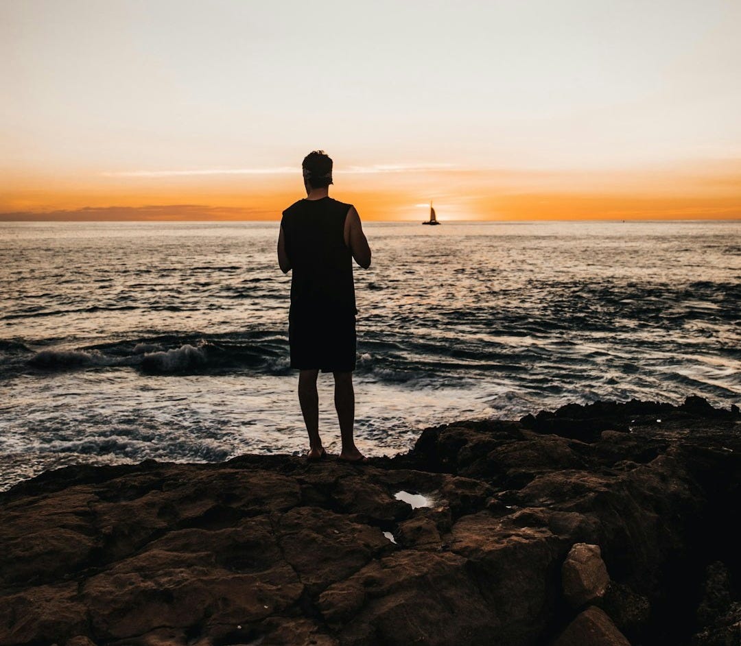 silhouette of man standing on rocky shore during sunset