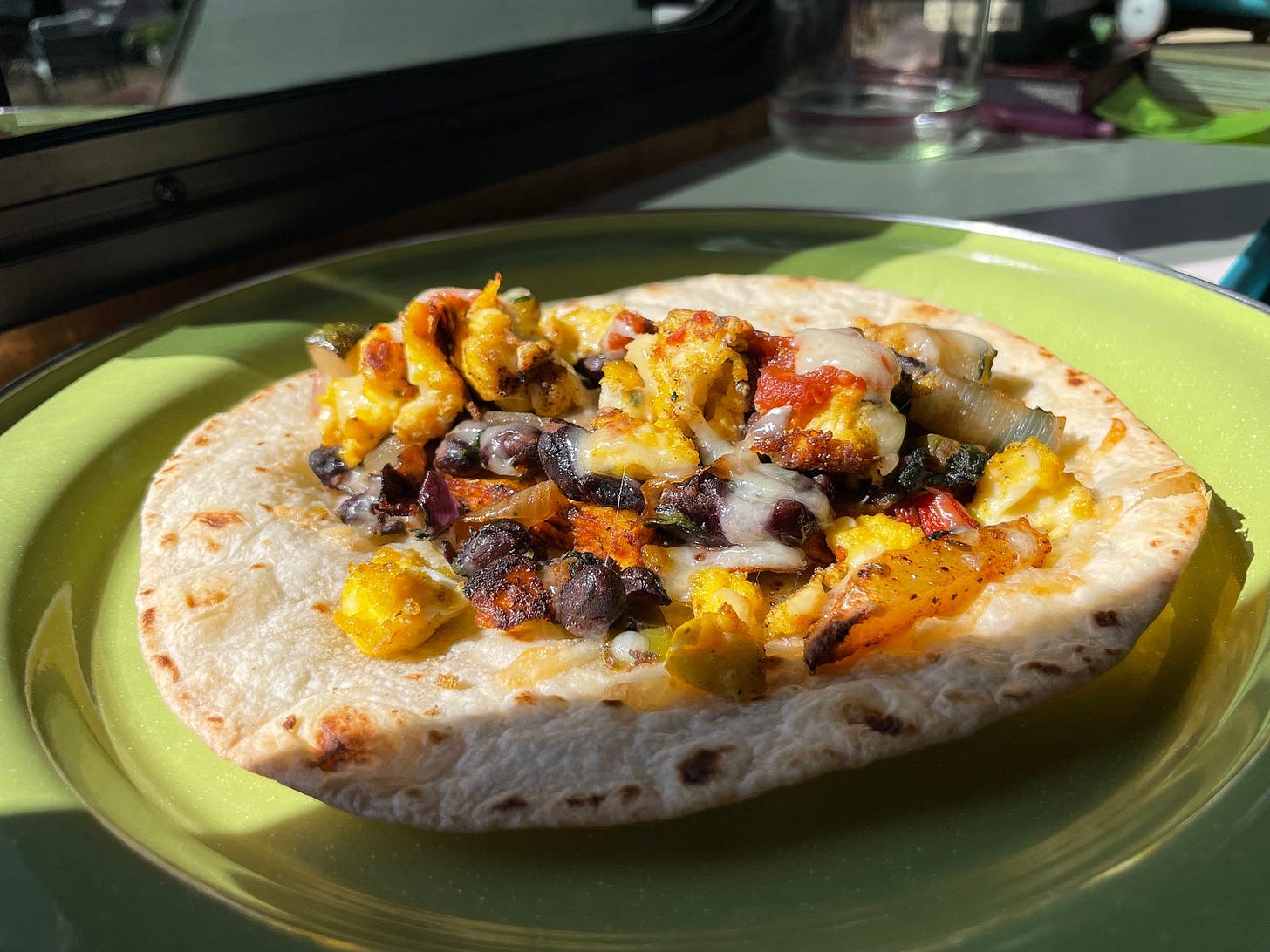 a plate with a crispy tortilla covered in beans, eggs, cheese, and soft potatoes