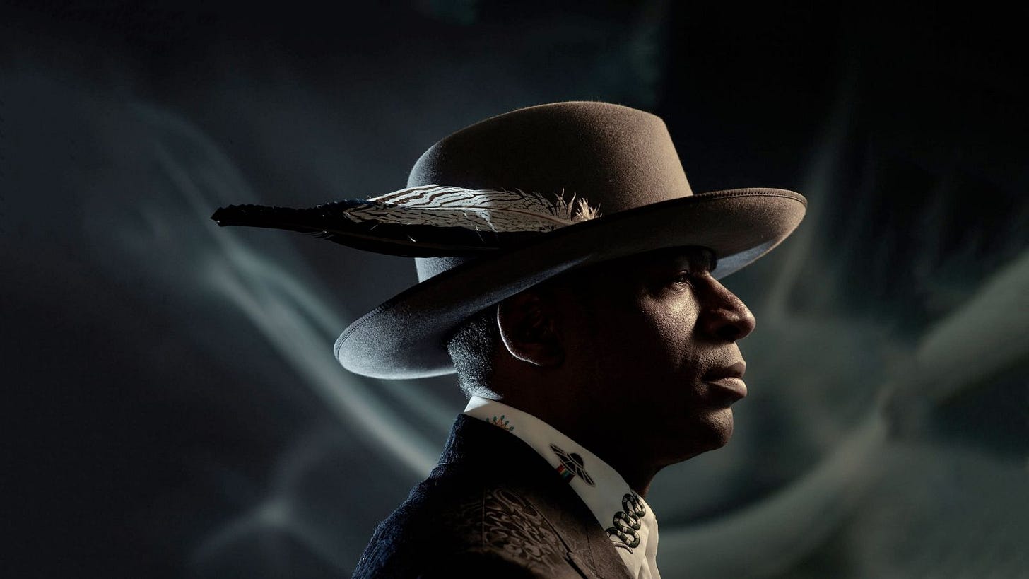 Ray Angry in profile, feathered wide-brim hat against dark smoke — pianist and producer of The Roots.