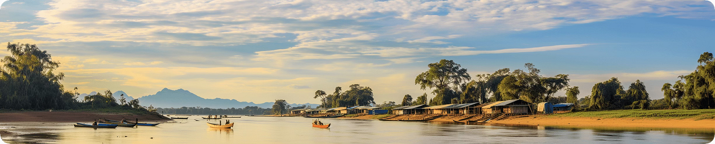 Daytime riverside scene with boats, wooden houses, and distant Cambodian mountains under a blue sky.
