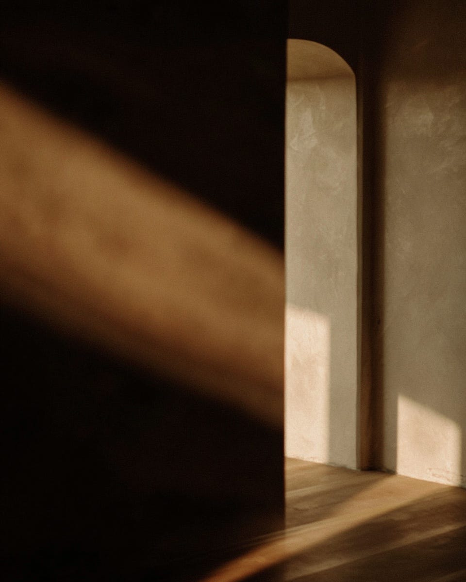 Atmospheric editorial photograph — warm archway cross light — lead image for The Room essay 'Some Things People Never Leave' by Chelsea Johnson, Chelsea + Co.