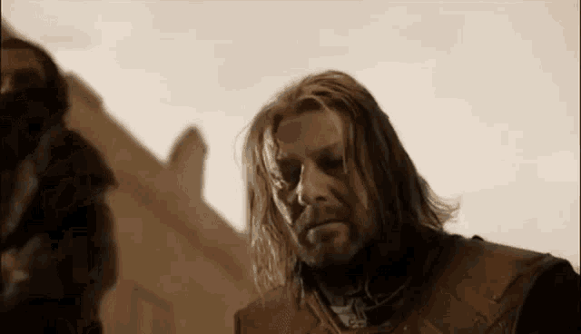 a man with long hair and a beard is standing in front of a building and looking at something .