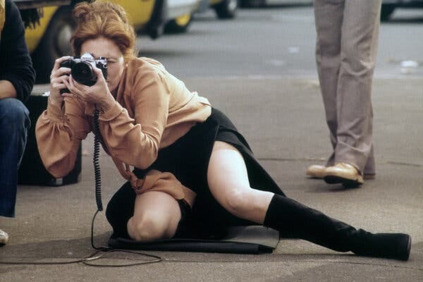 Faye Dunaway leans to the ground holding a camera.