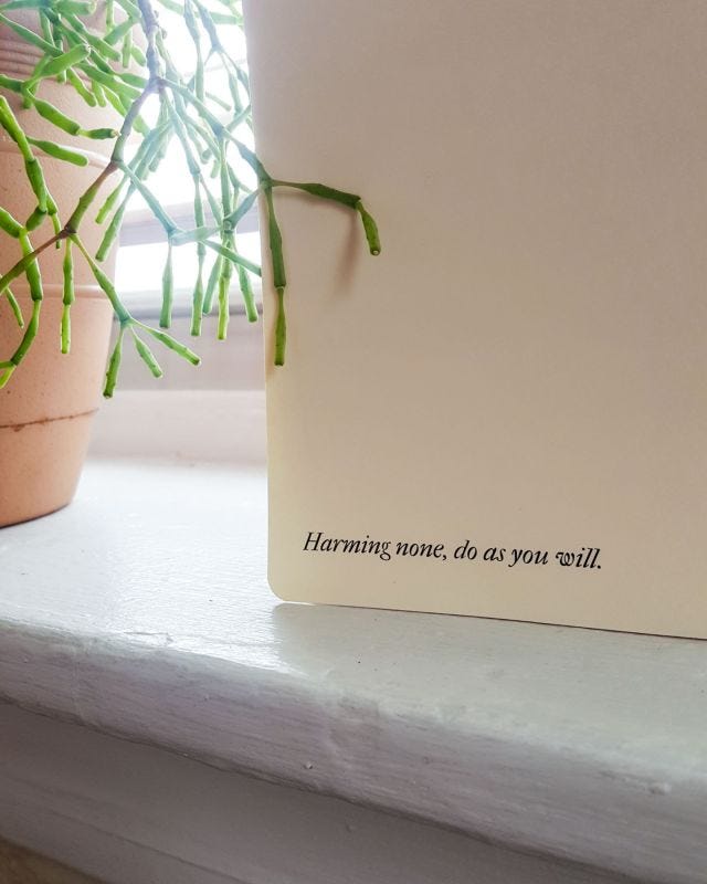 A close up shot of the back cover, an off-white card stock with rounded edges. Some serif text says Harming none, do as you will.