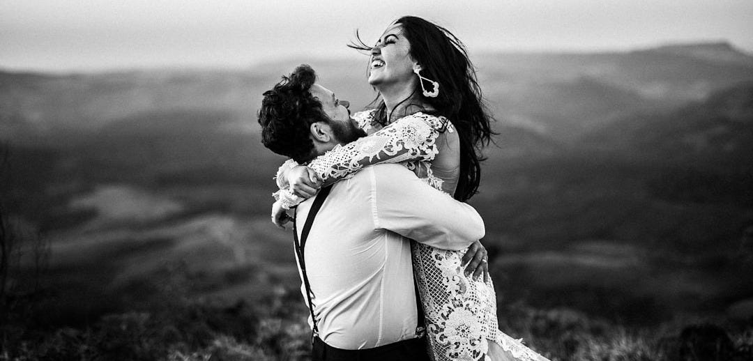 grayscale photography of man and woman hugging near hill