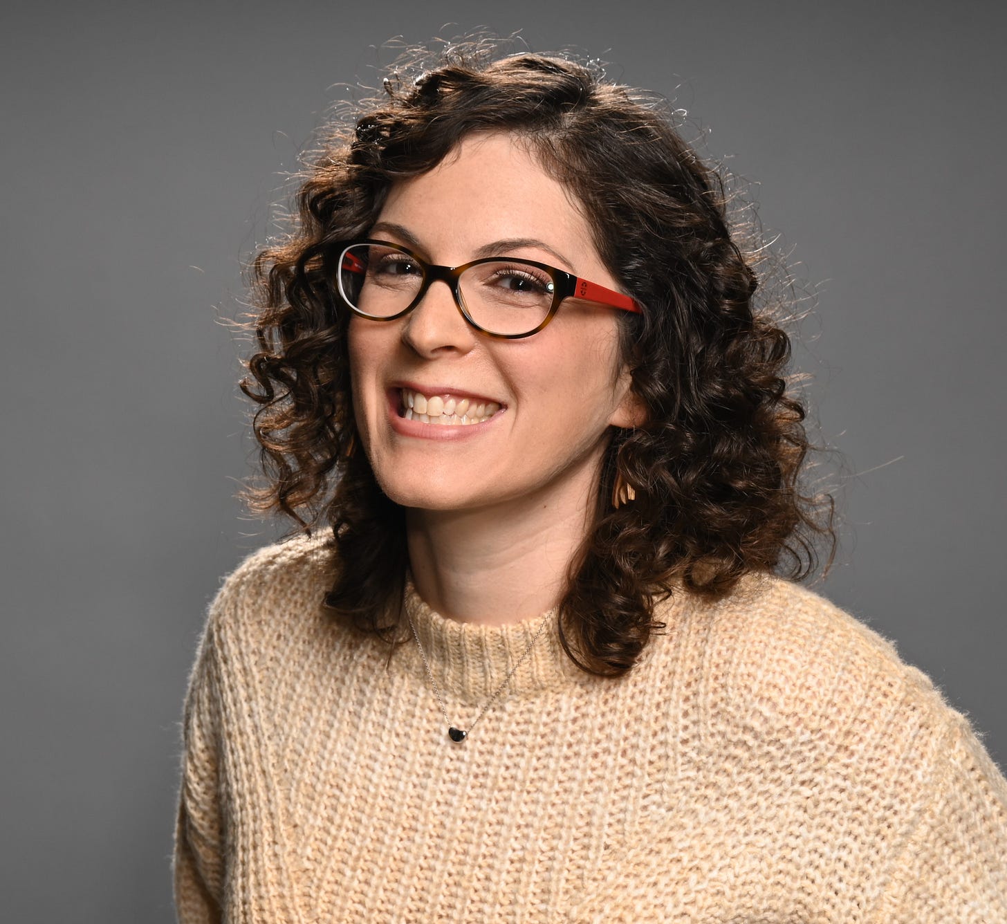 Becky Krystal, a white woman with shoulder-length curly brown hair and glasses wearing an offwhite sweater