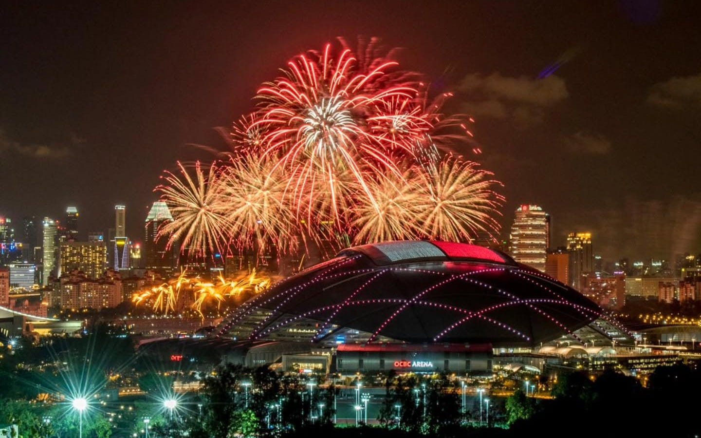 A wide view of the Singapore skyline and the National Stadium glowing under fireworks during the 2026 National Day Parade celebrations at Kallang. A wide view of the Singapore skyline and the National Stadium glowing under fireworks during the 2026 National Day Parade celebrations at Kallang.