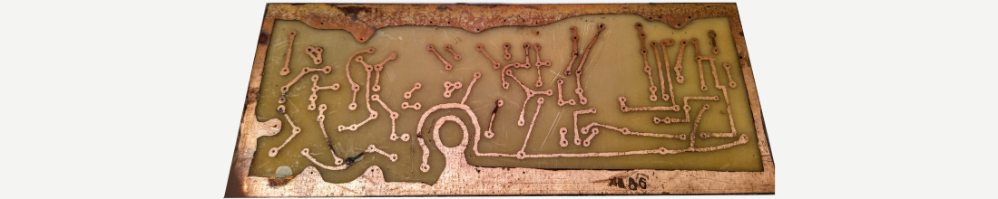 Hand-etched single-layer PCB from 1986 with exposed copper traces and drilled through-holes. Hand-etched single-layer PCB from 1986 with exposed copper traces and drilled through-holes.