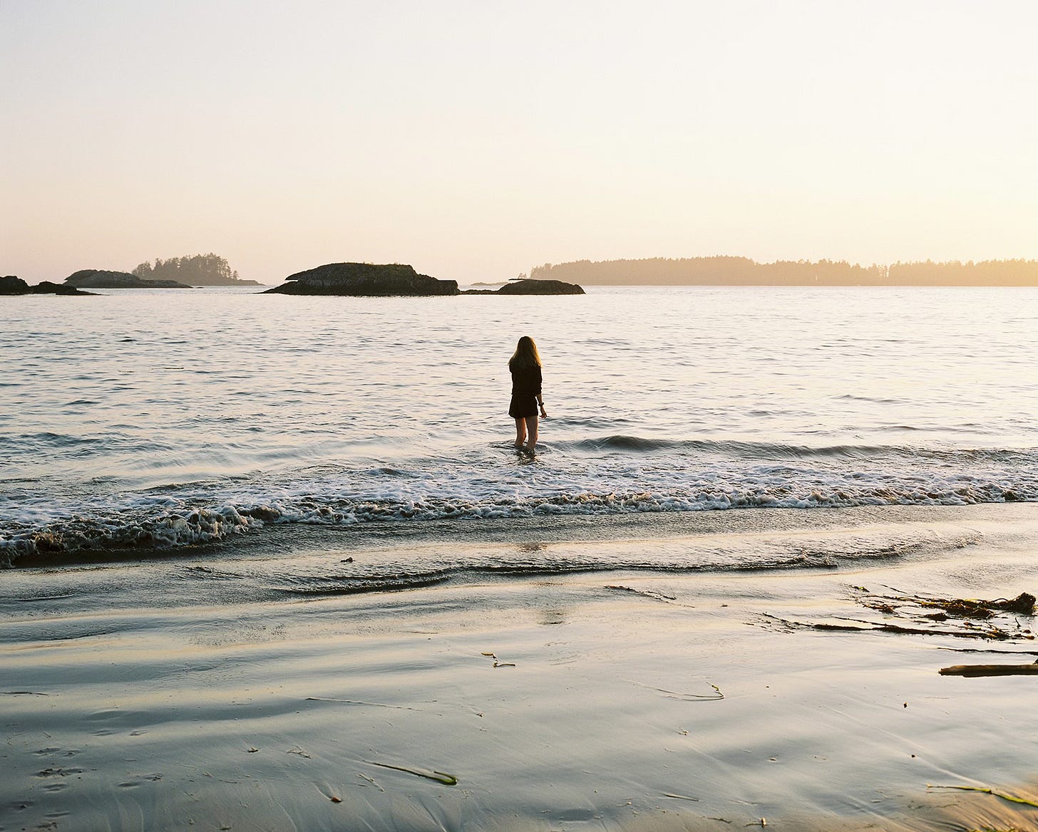 Figure standing in the sea looking out at a fading sun