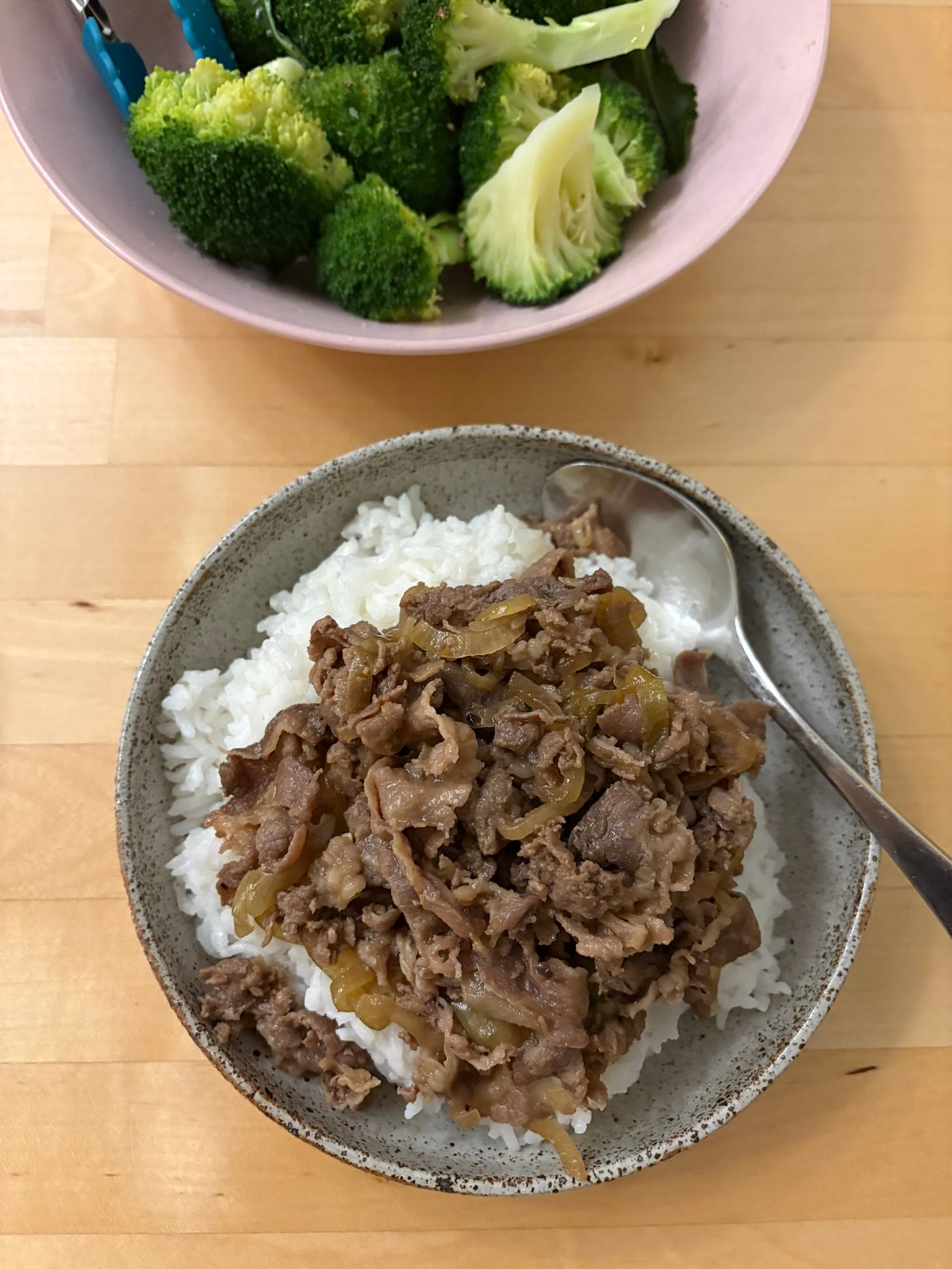 A bowl of white rice topped with bulgogi beef. Steamed broccoli in the background