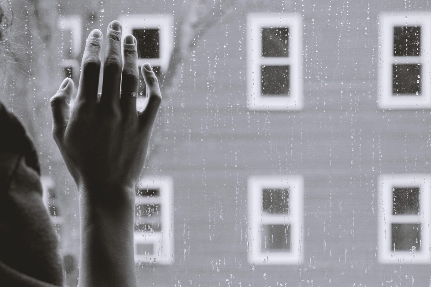 Hand resting on glass with rain outside on a gray day Hand resting on glass with rain outside on a gray day
