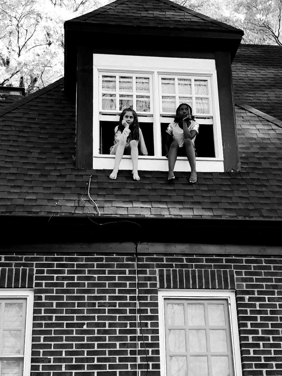 two girls sitting on white 2-panel windows during daytime