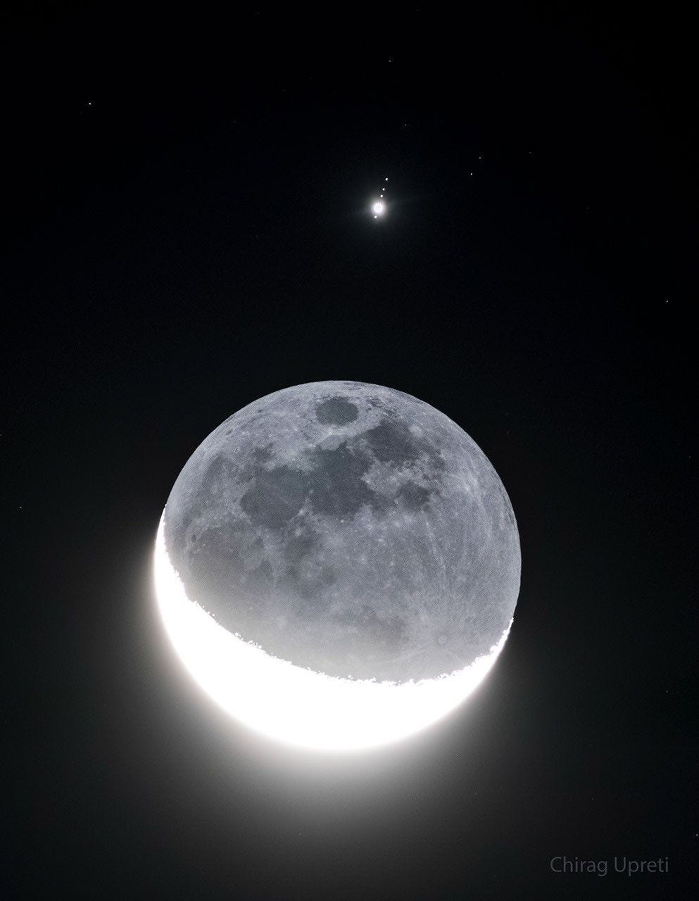 In front of a dark background an image of Earth's Moon appears with a lower crescent brightly lit. The rest of the Moon is also faintly visible. Above the Moon is a bright point of light surrounded by four fainter points of light in row. Please see the explanation for more detailed information. In front of a dark background an image of Earth's Moon appears with a lower crescent brightly lit. The rest of the Moon is also faintly visible. Above the Moon is a bright point of light surrounded by four fainter points of light in row. Please see the explanation for more detailed information.
